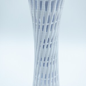 May include: A white, 3D printed vase with a lattice design. The vase is tall and slender, with a cylindrical shape. The lattice design is made up of a series of intersecting lines that create a geometric pattern.