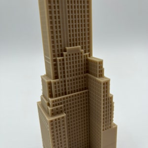 May include: A detailed 3D printed model of a skyscraper, featuring a beige color and a textured facade. The model is a miniature representation of a tall building with multiple floors and a rectangular shape.