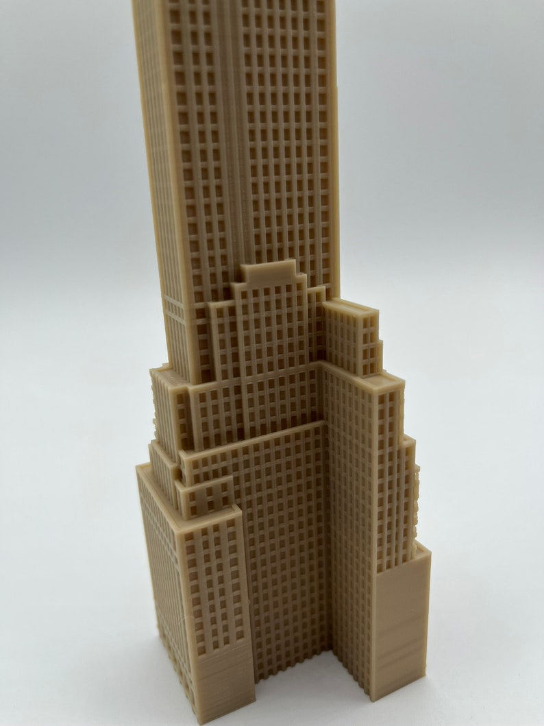 May include: A detailed 3D printed model of a skyscraper, featuring a beige color and a textured facade. The model is a miniature representation of a tall building with multiple floors and a rectangular shape.