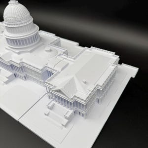 K&ouml;nnte beinhalten: Ein wei&szlig;es Architekturmodell des US-Kapitolgeb&auml;udes. Das Modell zeigt detaillierte Merkmale der Kuppel, der S&auml;ulen und der Gesamtstruktur. Das Modell befindet sich vor einem schwarzen Hintergrund.