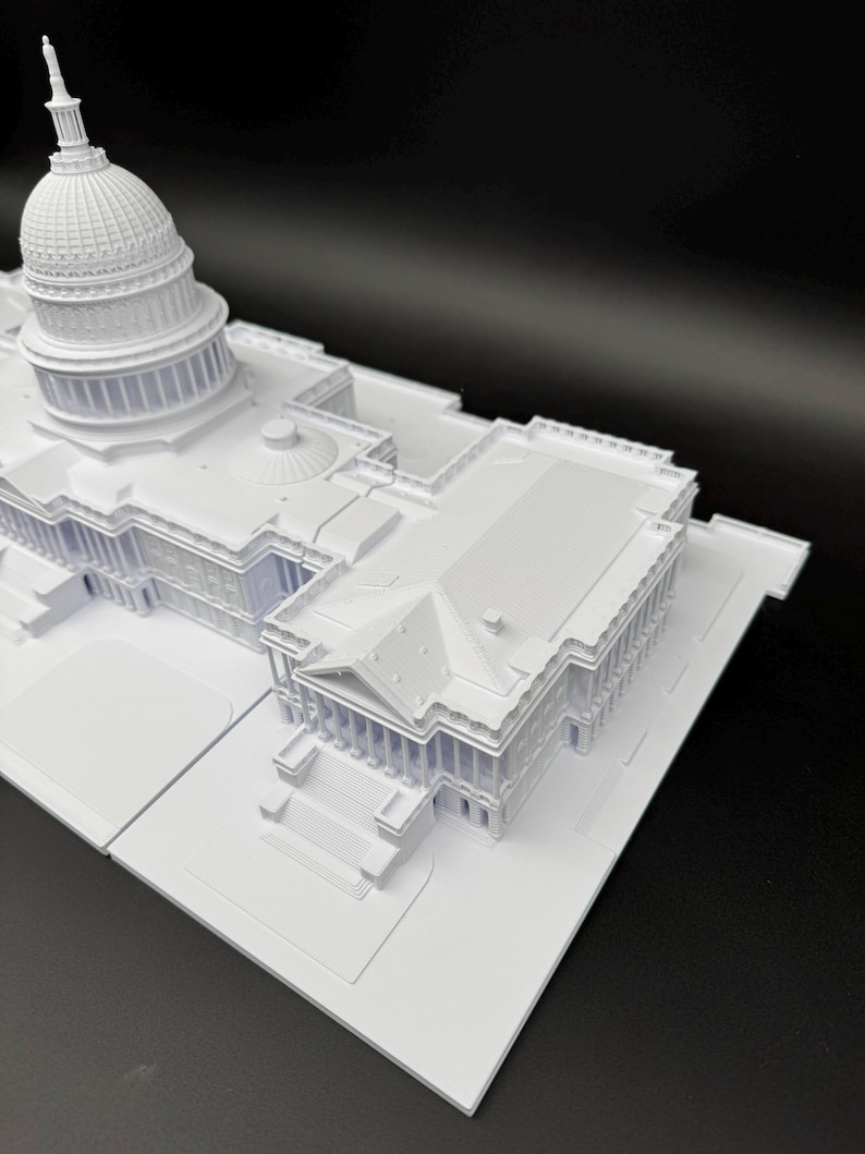 K&ouml;nnte beinhalten: Ein wei&szlig;es Architekturmodell des US-Kapitolgeb&auml;udes. Das Modell zeigt detaillierte Merkmale der Kuppel, der S&auml;ulen und der Gesamtstruktur. Das Modell befindet sich vor einem schwarzen Hintergrund.