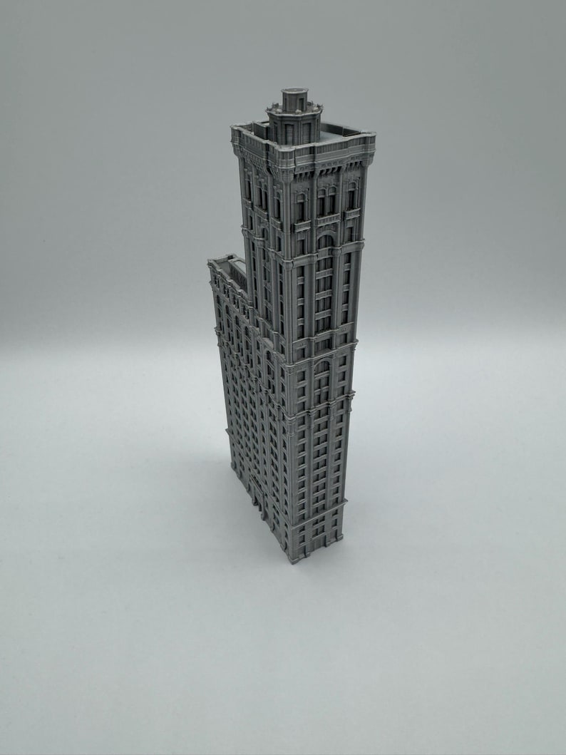 May include: A grey, 3D-printed model of a tall skyscraper. The building has many windows and architectural details, including a decorative top. The model is standing upright against a plain background.
