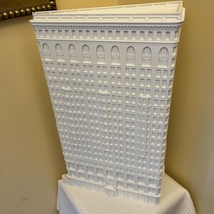 Puede incluir: Un modelo 3D impreso en blanco de un edificio alto con muchas ventanas. El edificio tiene una fachada detallada con arcos y molduras decorativas.