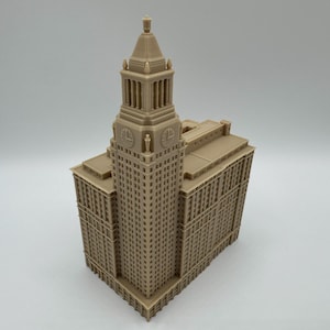 May include: A tan-colored architectural model of a tall building with a clock tower. The building has many windows and detailed architectural features. The model is set against a plain background.