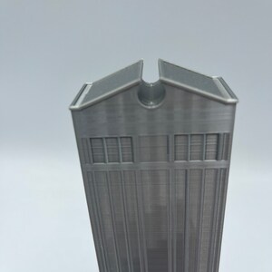May include: A gray 3D printed model of a tall building with a flat roof and a small opening at the top.