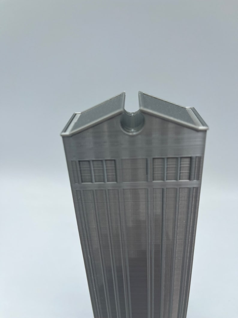 May include: A gray 3D printed model of a tall building with a flat roof and a small opening at the top.