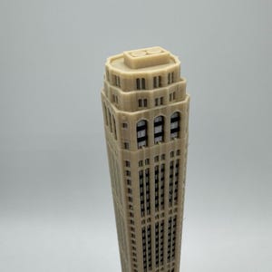 Op de afbeelding: Een beige 3D-geprint model van een hoge wolkenkrabber met veel ramen.