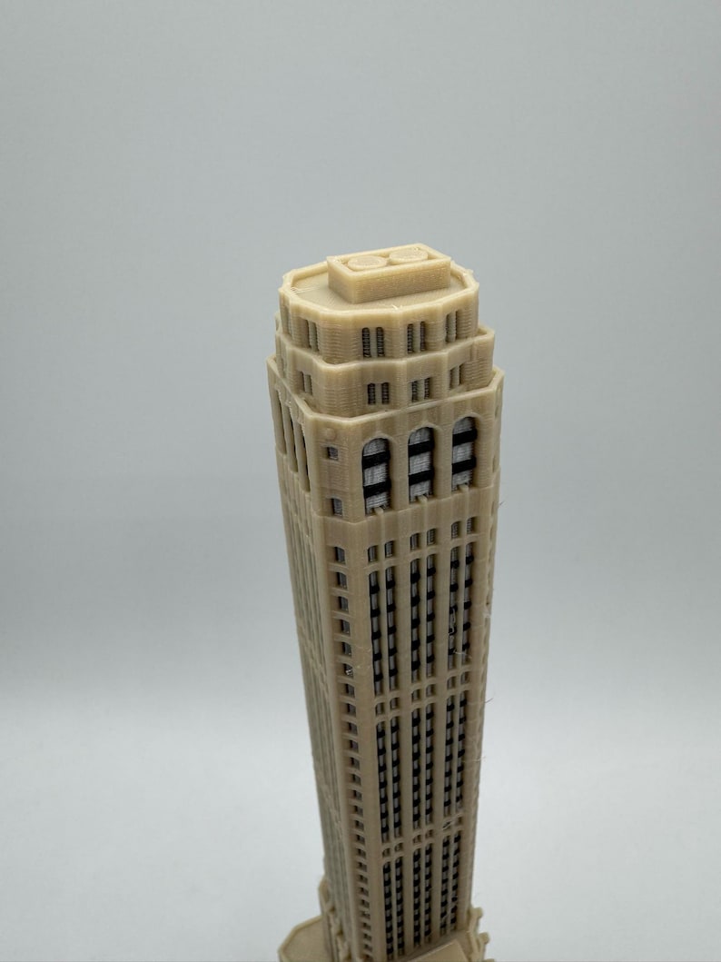 Op de afbeelding: Een beige 3D-geprint model van een hoge wolkenkrabber met veel ramen.