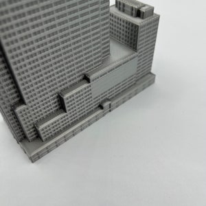 May include: A gray 3D printed model of a skyscraper with a detailed facade and a smaller building attached to the side.