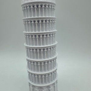 May include: A white 3D printed model of the Leaning Tower of Pisa. The model is detailed with arches and columns.