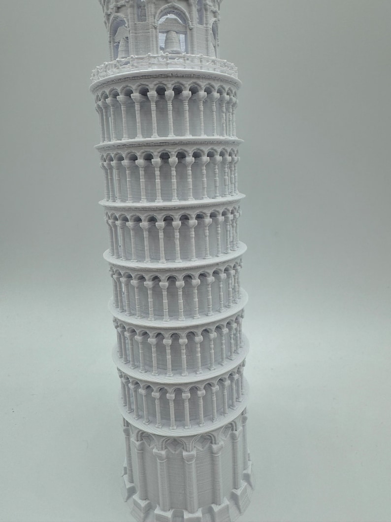 May include: A white 3D printed model of the Leaning Tower of Pisa. The model is detailed with arches and columns.