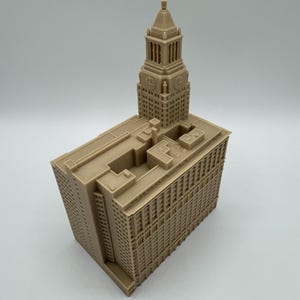 May include: A tan-colored architectural model of a building with a clock tower. The model has detailed windows and architectural features. The building is rectangular with a tall clock tower on top.