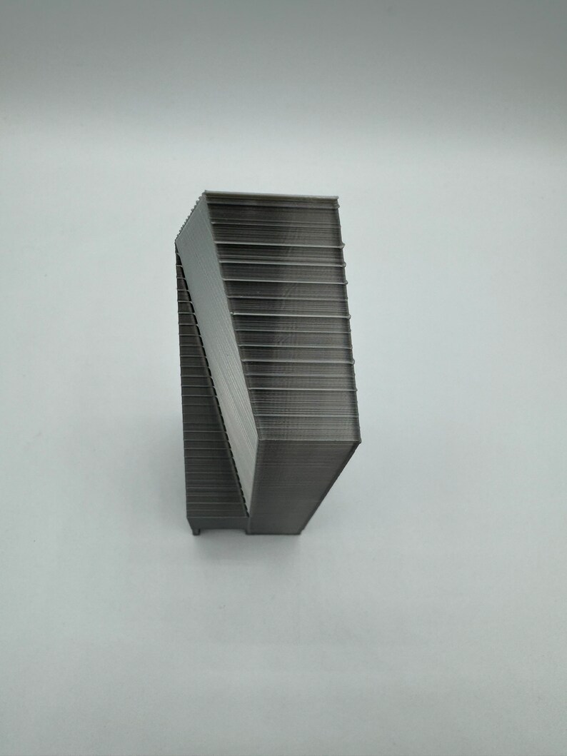 May include: A gray, 3D printed object with a geometric shape. The object is made up of many layers, creating a textured surface.