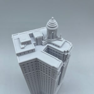 Op de afbeelding: Wit 3D-geprint model van een hoog gebouw met een koepelvormig dak.