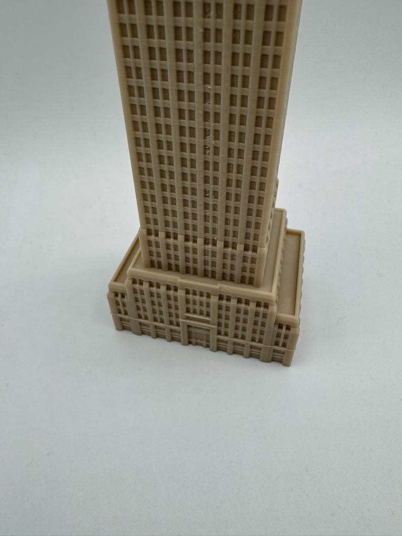 Puede incluir: Un modelo de pl&aacute;stico beige de un rascacielos alto con muchas ventanas. El modelo est&aacute; detallado con una base y un techo.