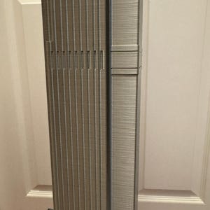 K&ouml;nnte beinhalten: Detailliertes Modell eines Wolkenkratzers mit strukturierter, metallischer Oberfl&auml;che. Die Fassade des Geb&auml;udes weist vertikale Linien und vertiefte Abschnitte mit rechteckiger Basis auf. Das Modell steht vor einem neutralen Hintergrund.