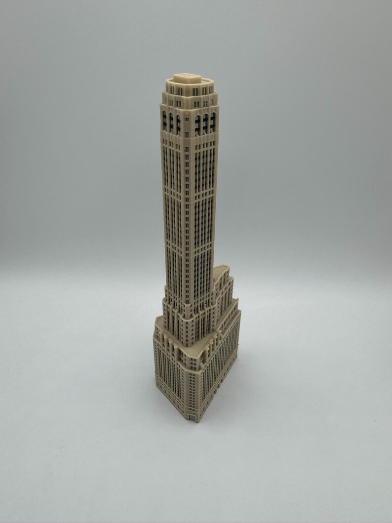 Op de afbeelding: Een gedetailleerd miniatuurmodel van een hoge, beige wolkenkrabber met veel ramen. Het model is gemaakt van plastic en heeft een licht getextureerd oppervlak.