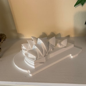 May include: A white miniature model of the Sydney Opera House on a white base. The model is made of plastic and is about 6 inches tall.