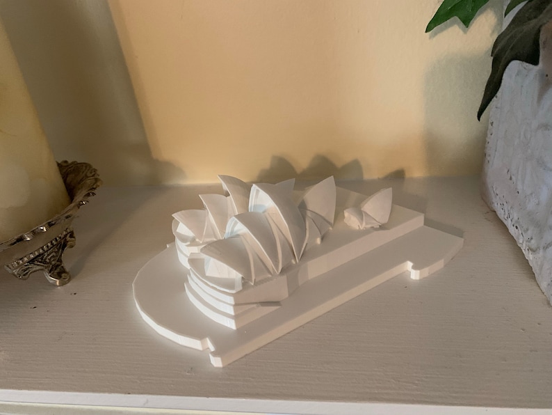 May include: A white miniature model of the Sydney Opera House on a white base. The model is made of plastic and is about 6 inches tall.
