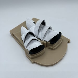 May include: A white 3D printed model of the Sydney Opera House on a brown base.