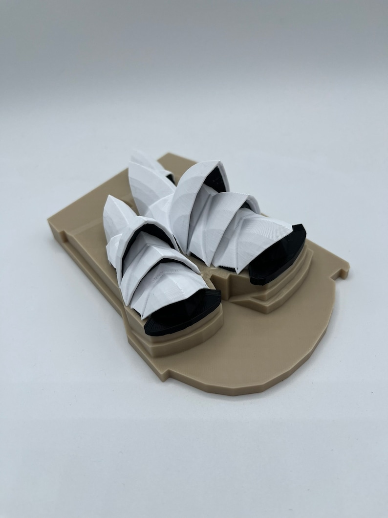 May include: A white 3D printed model of the Sydney Opera House on a brown base.