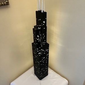 May include: A black LEGO model of the Willis Tower, also known as the Sears Tower, with white lights and a white cord. The model is on a white surface.