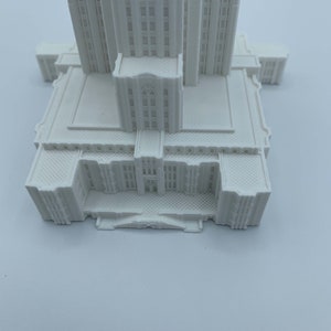 May include: White 3D printed model of a tall building with a detailed facade and a flat roof.