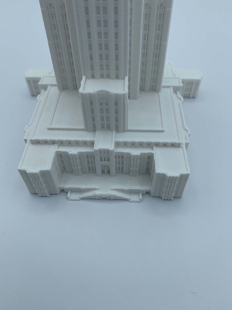 May include: White 3D printed model of a tall building with a detailed facade and a flat roof.