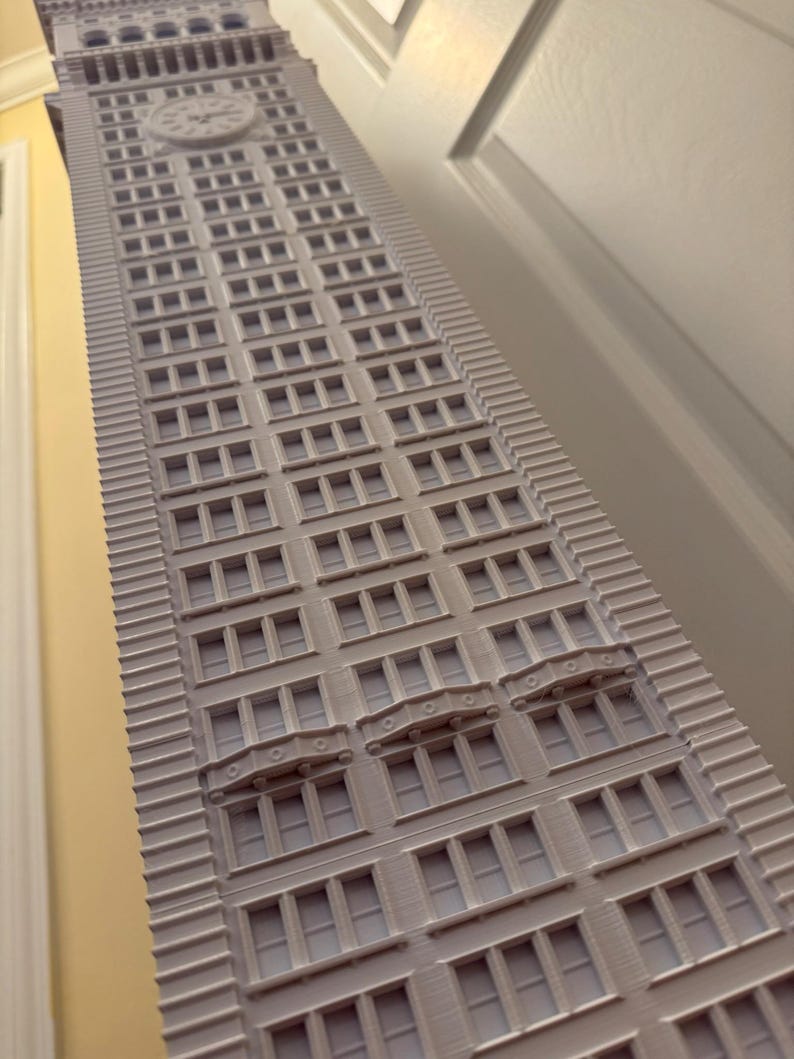 Op de afbeelding: Een wit 3D-geprint model van een hoog gebouw met veel ramen en decoratieve details. Het gebouw heeft een klok op de bovenkant.
