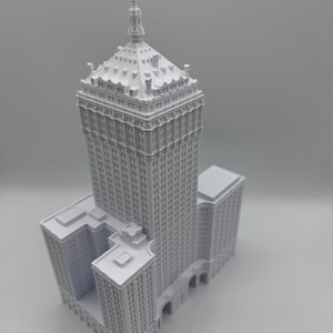 Puede incluir: Una miniatura gris detallada de un rascacielos con un dise&ntilde;o de varios niveles. El edificio presenta numerosas ventanas, detalles arquitect&oacute;nicos y una parte superior puntiaguda. El modelo est&aacute; sobre un fondo liso.
