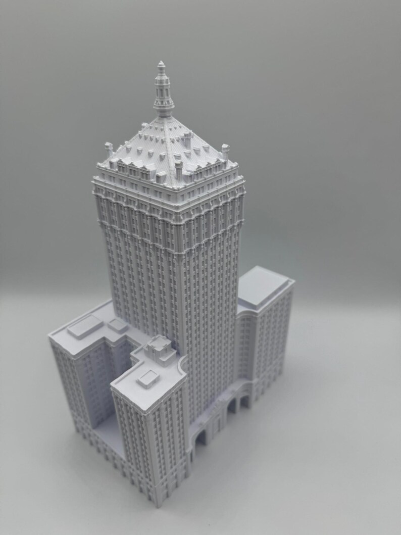 Puede incluir: Una miniatura gris detallada de un rascacielos con un dise&ntilde;o de varios niveles. El edificio presenta numerosas ventanas, detalles arquitect&oacute;nicos y una parte superior puntiaguda. El modelo est&aacute; sobre un fondo liso.