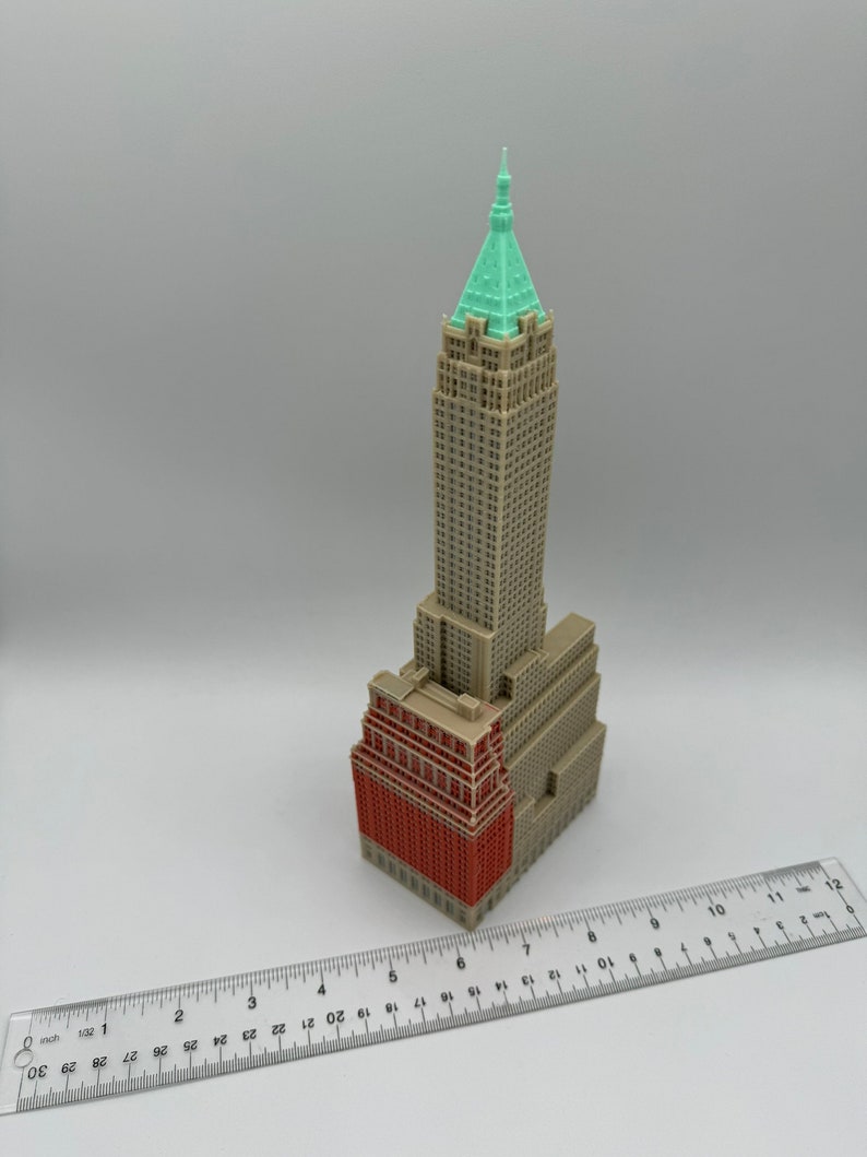 May include: A 3D printed model of a skyscraper with a green roof and a red brick facade. The model is approximately 15 cm tall and is sitting on a white surface.