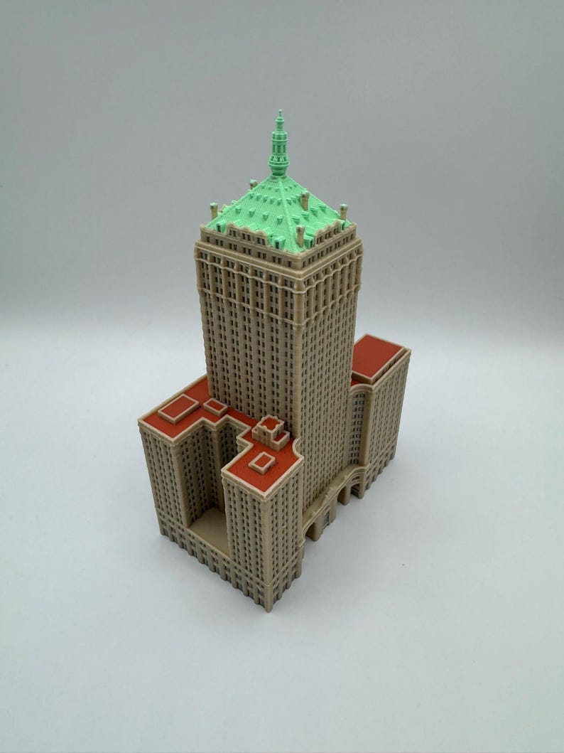 May include: A detailed miniature model of a skyscraper. The building features a tan facade, a green roof, and red accents. The model is a replica of a classic architectural design.
