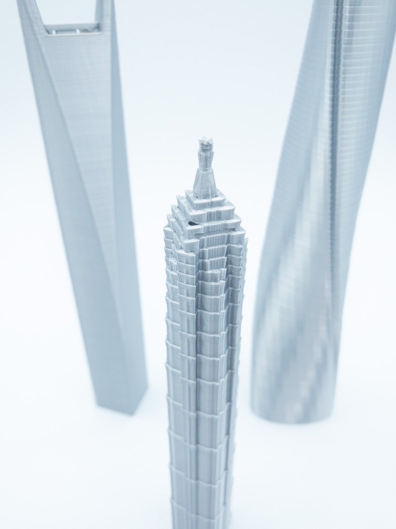 May include: A silver 3D printed model of a skyscraper with a pointed top. The model is surrounded by two other silver 3D printed skyscrapers.