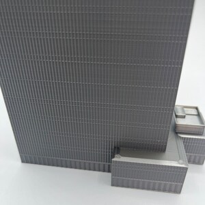 May include: A gray, detailed model of a skyscraper with a textured facade. The model is made of plastic and has a realistic design.