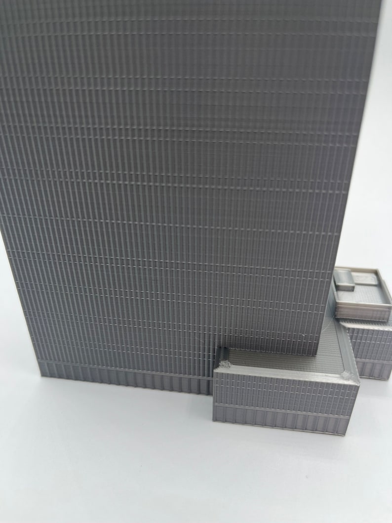 May include: A gray, detailed model of a skyscraper with a textured facade. The model is made of plastic and has a realistic design.