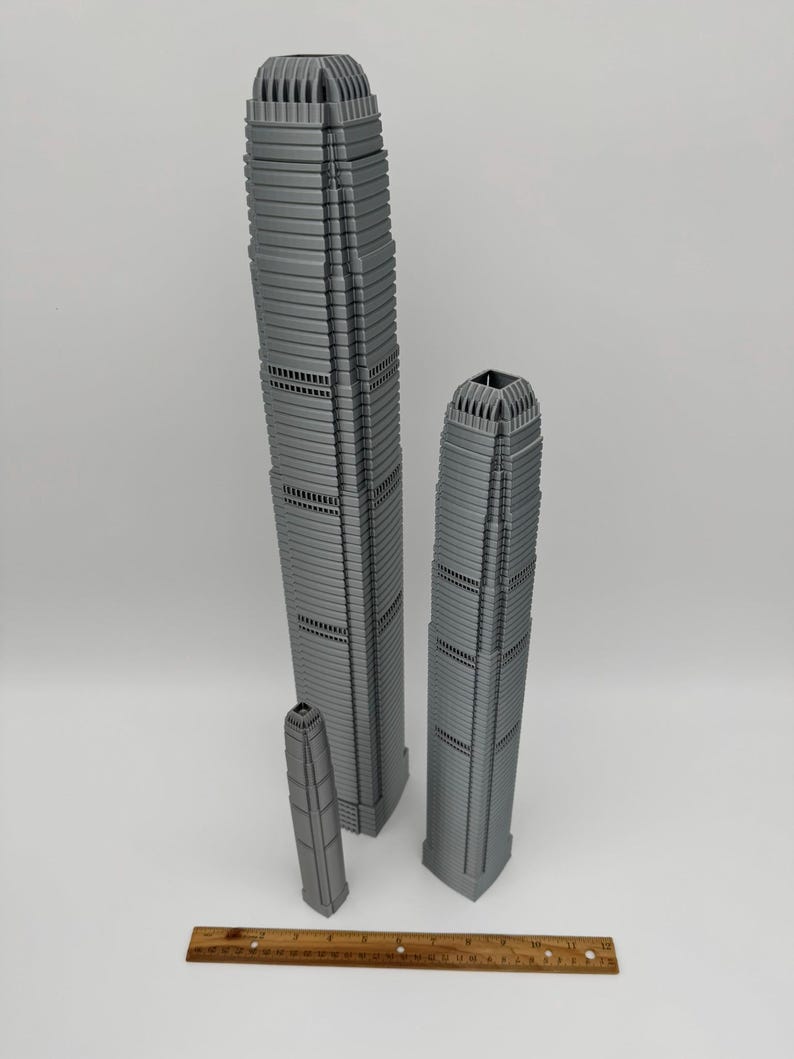 May include: Three gray miniature skyscraper models of varying heights. The tallest model is approximately 12 inches tall, the next is about 9 inches, and the smallest is around 4 inches. A wooden ruler is at the bottom.