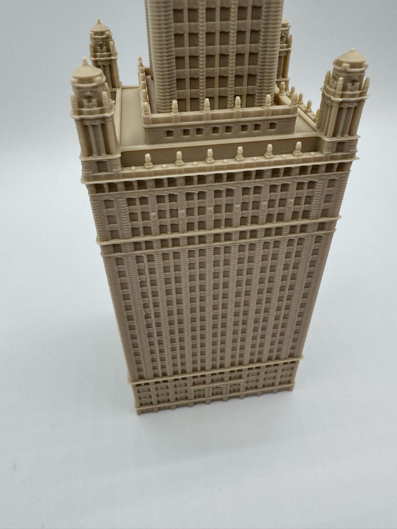 May include: A beige architectural model of a tall building with intricate details. The model features multiple levels, windows, and decorative elements, showcasing a classic skyscraper design. The building has a rectangular base and a central tower.