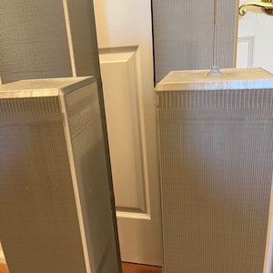 Pu&ograve; includere: Modelli in miniatura delle Torri Gemelle, di colore grigio chiaro, con dettagli a coste verticali. I modelli sono posizionati davanti a una porta bianca e un tappeto marrone.