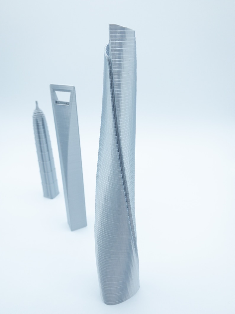 May include: Three silver 3D printed models of skyscrapers. The tallest model is a twisted tower with a smooth, curved surface. The other two models are more traditional, with straight lines and a rectangular shape.