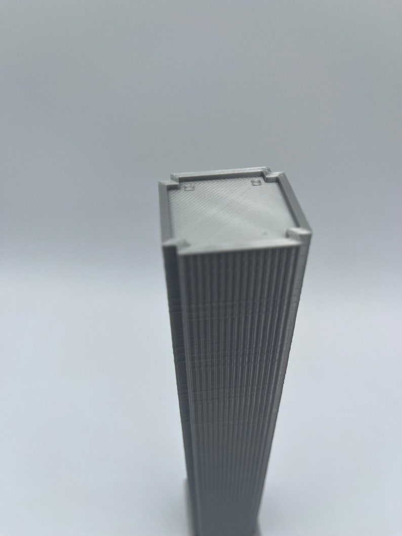 Op de afbeelding: Een grijs 3D-geprint model van een wolkenkrabber met een plat dak en een getextureerde gevel.
