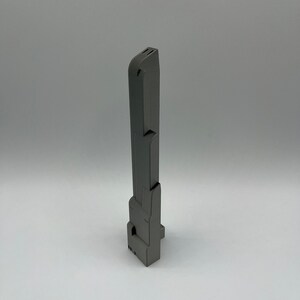 May include: A gray, rectangular, vertical object with a series of geometric shapes and cutouts. The object appears to be made of a solid material and has a matte finish. The design is modern and industrial.
