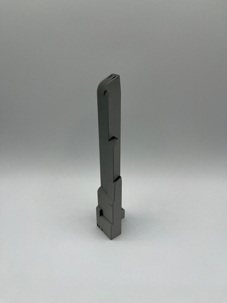 May include: A gray, rectangular, vertical object with a series of geometric shapes and cutouts. The object appears to be made of a solid material and has a matte finish. The design is modern and industrial.