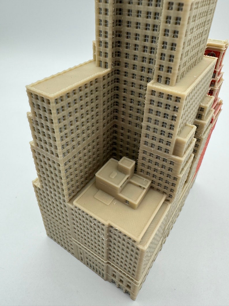 May include: A detailed 3D printed model of a tall beige building with multiple windows and a flat roof. The building has a slightly angled roof and a small rectangular structure on the top.