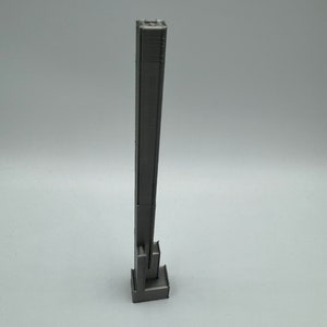 Op de afbeelding: Een 3D-geprint model van een hoog, slank gebouw met een rechthoekige basis. Het gebouw is grijs en heeft een getextureerd oppervlak.
