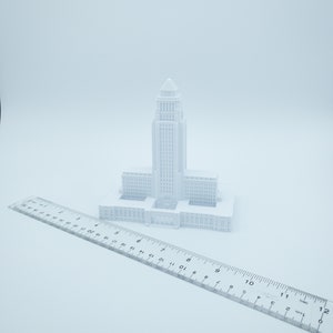 May include: A white 3D printed model of a city hall building. The model is about 6 inches tall and is sitting on a white ruler.
