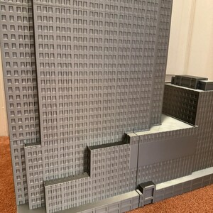 May include: A detailed, gray architectural model of a skyscraper, featuring numerous windows and a multi-tiered design. The model showcases the building's facade with precise detailing, including recessed windows and a textured surface.
