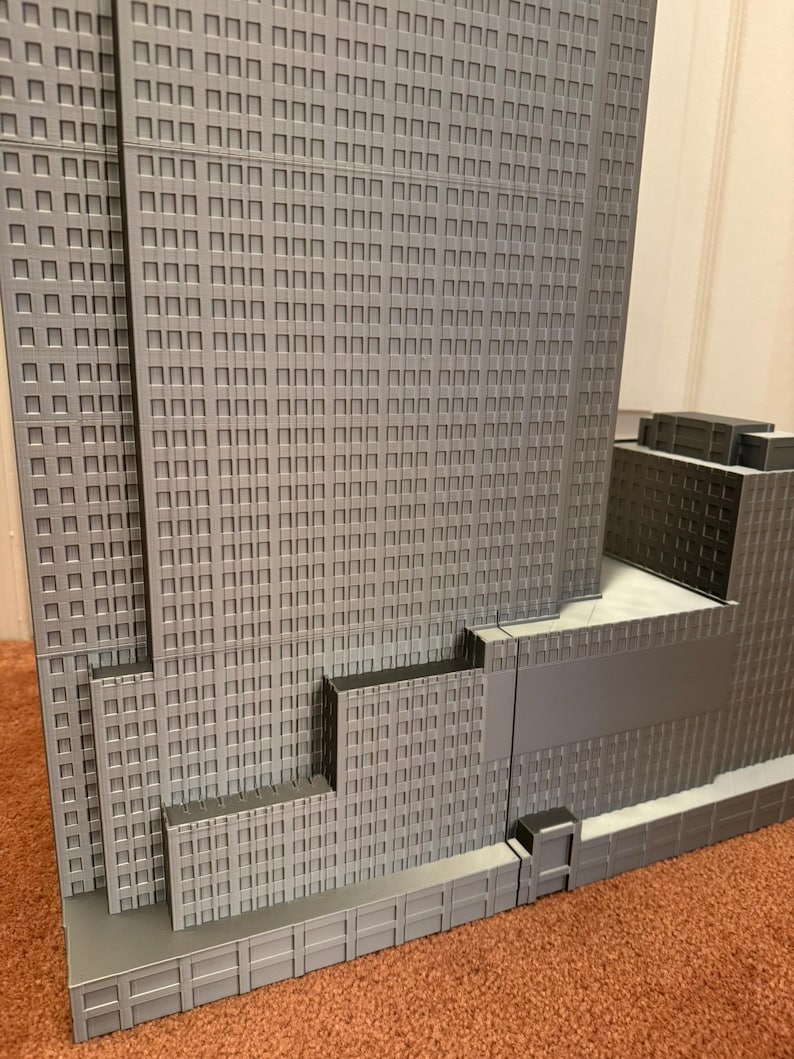 May include: A detailed, gray architectural model of a skyscraper, featuring numerous windows and a multi-tiered design. The model showcases the building's facade with precise detailing, including recessed windows and a textured surface.