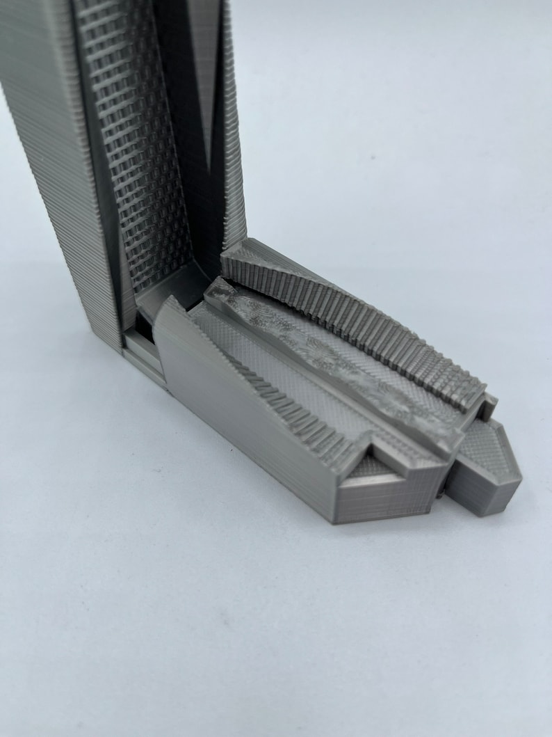 May include: A 3D printed model of a building with a textured surface and a geometric design. The model is made of gray plastic and has a sharp, angular shape.