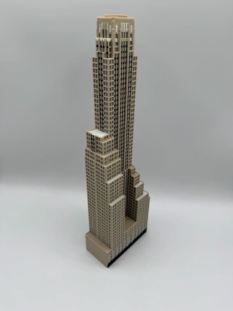May include: A beige miniature skyscraper model with a detailed facade. The building has a stepped design, with a tall central tower and multiple smaller sections. The model is set against a plain white background.